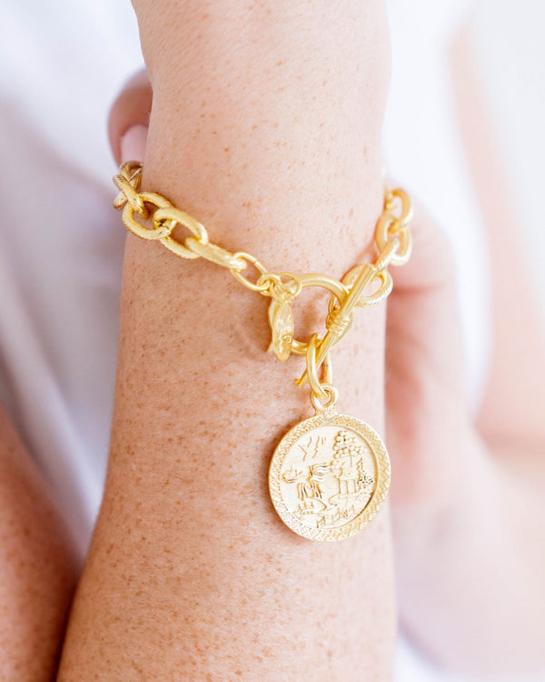 A person wearing a 24k gold triple-plated Blue Willow toggle bracelet with a round coin pendant.