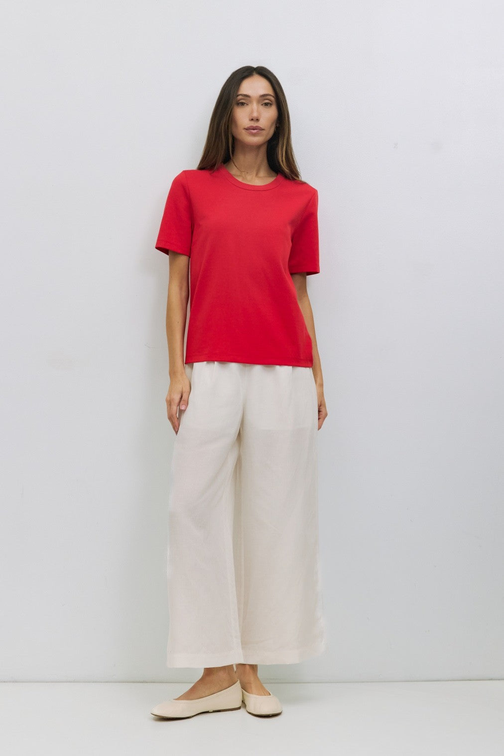 Woman wearing a red short-sleeve cotton blend t-shirt and loose-fit off-white linen pants.