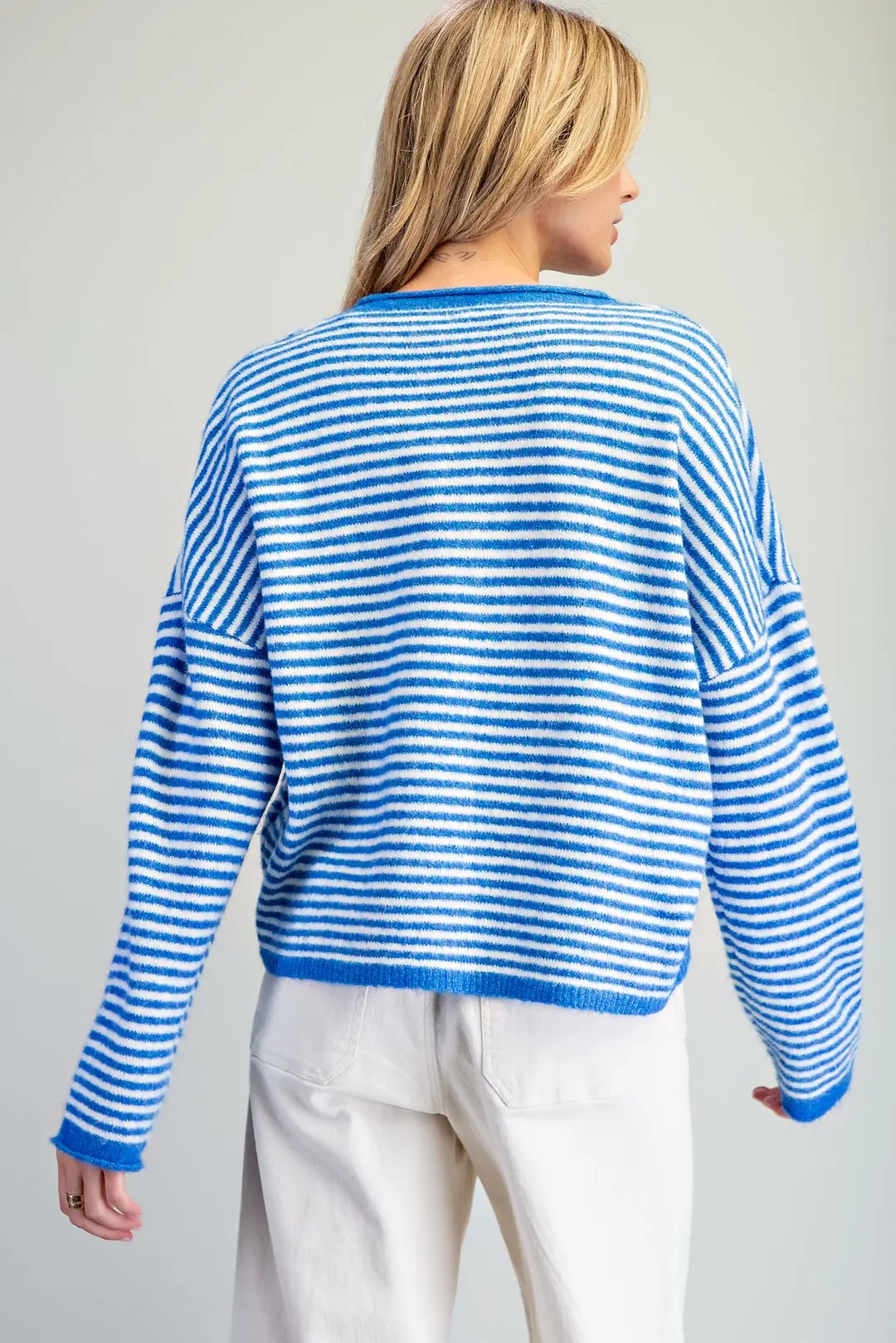 Back view of a woman wearing a blue and white horizontal striped knit cardigan with white pants.