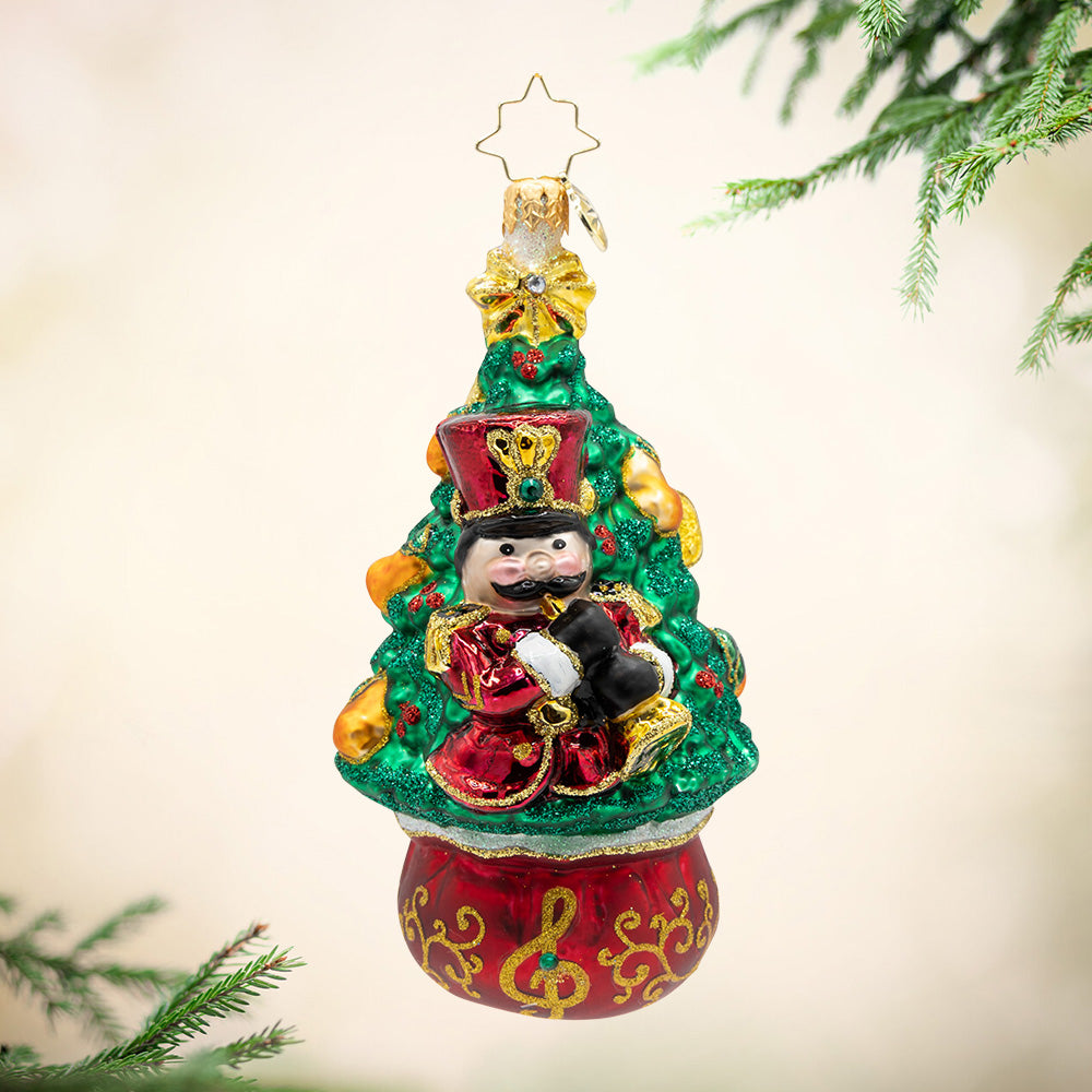 Glass Christmas tree ornament featuring a nutcracker piper on a red base with a gold treble clef.