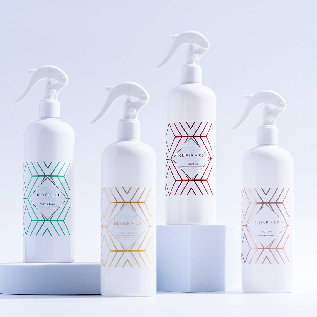Four white Oliver + Co Multi-Purpose Cleaner spray bottles with geometric designs in various colors.