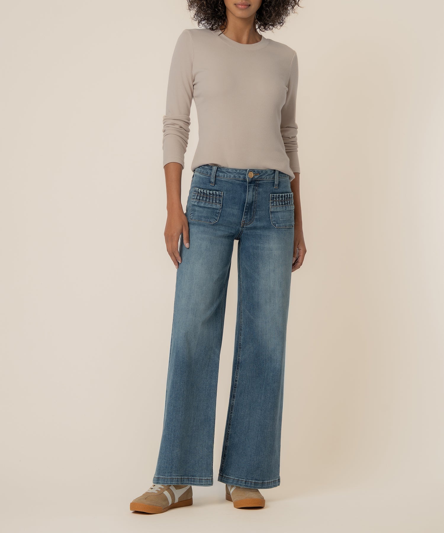 Woman wearing Maya high rise wide leg jeans with ruched patch pockets and a beige long sleeve top.