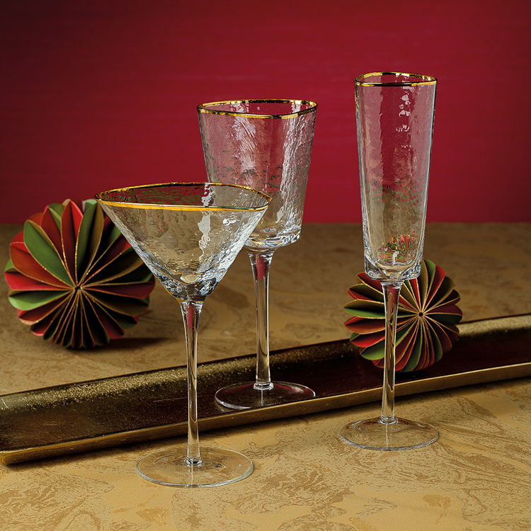 Aperitivo triangular martini glass with a gold rim and hammered texture on a gold surface.