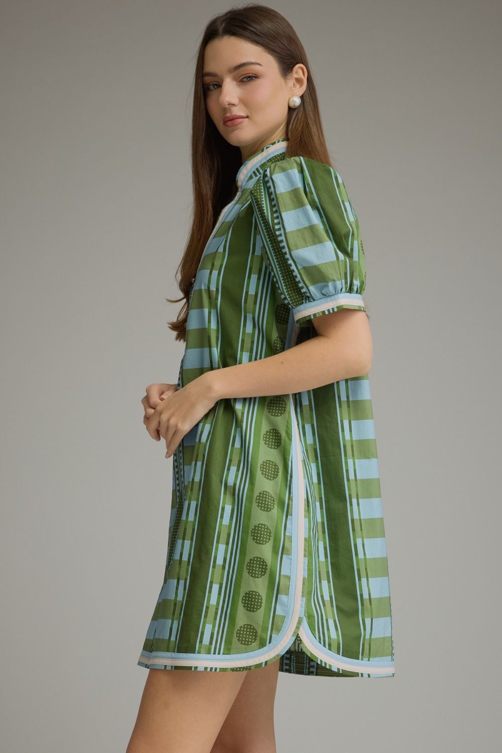 Side view of a woman wearing a green and blue striped mini dress with short puff sleeves.