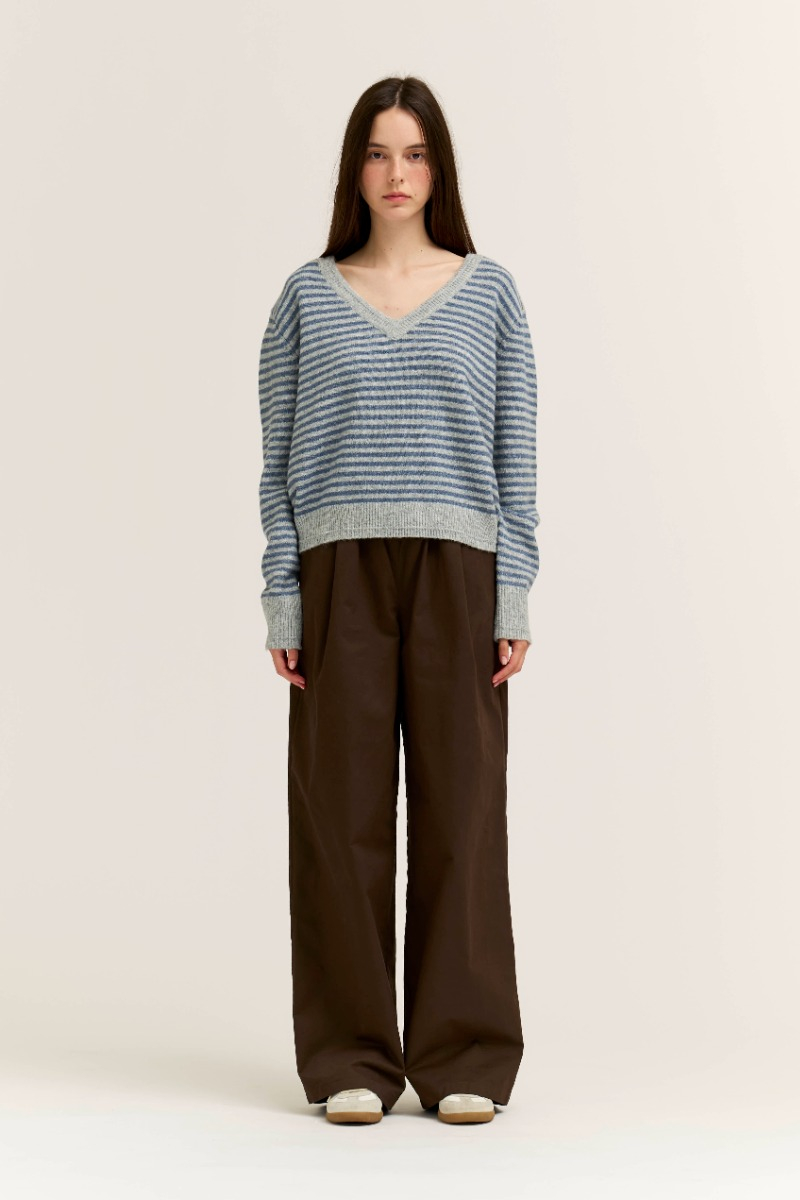 Woman wearing the Sienna Striped V-Neck Sweater in blue and gray with brown wide-leg trousers.