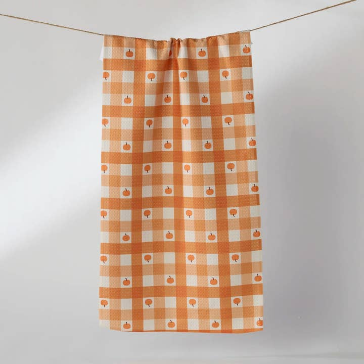 Orange and white checkered waffle weave tea towel with small pumpkin patterns hanging on a line.